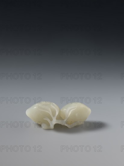 Paperweight - peaches; maker, Chinese; peaches iconography; Qianlong 1736–1795 style; Qing 1644–1911; dated 1736–1795; China; paperweight; height 5.7 cm, width 3.4 cm., A smooth, pale off-white organic-shaped object rests on a smooth gray surface with a soft shadow beneath it; the object appears to have two lobes connected by translucent white, branch-like veins, and the background transitions from light gray near the surface to dark gray-black toward the top.