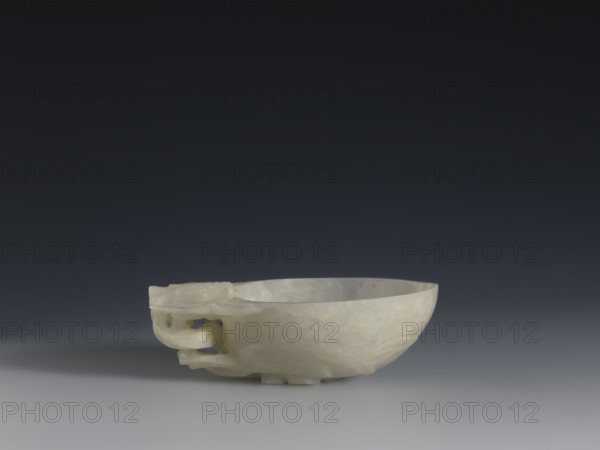 A vessel for rinsing brushes, Chinese, Qing dynasty 1644–1911, 19th century. Painted decoration of peaches iconography; painting implements. Vessel. Height 3.5 cm; width 11.0 cm; depth 7.4 cm., A smooth pale bowl with a creamy off-white color sits on a flat surface against a dark gray to black gradient background, showing a carved handle-like decorative element on one side and subtle translucent veining throughout the stone.