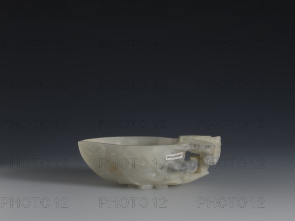 A vessel for rinsing brushes, creator unknown, Rubiec-Masalski, Fyodor Vasilyevich 1865-1920?, Tulisov, Jerzy 1943-, Chinese art, Chinese culture, Qing 1644-1911, painting implements, peaches iconographic, 19th century, China, vessel, height 3.5 cm, width 11.0 cm, depth 7.4 cm, A shallow, translucent bowl carved from pale stone with areas of white, cream, gray, and hints of yellow, shown resting on a smooth surface against a dark gray to nearly black gradient background; the bowl has a rounded rim and a carved handle-like protrusion with curving shapes and a few clouded inclusions in darker gray and beige tones, and the lighting creates soft shadows beneath and to the left of the object.