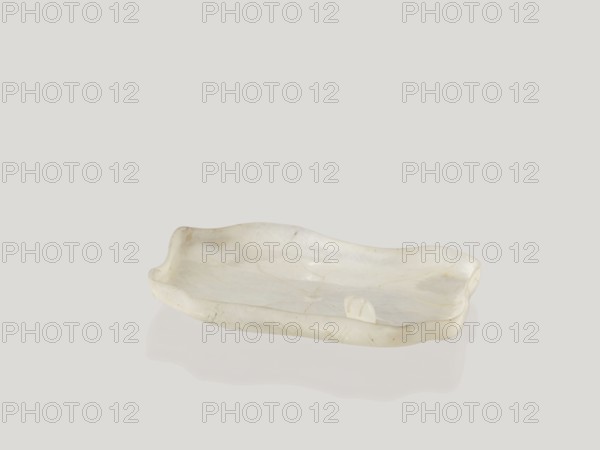 Ink vessel, Chinese, Qing 1644–1911, 18th–19th century, China; vessel used for painting implements; decorated with lotuses and calligraphy; height 0.7 cm, width 6.8 cm, depth 4.6 cm., A shallow irregularly shaped dish with wavy edges sits centered against a plain light gray background, appearing translucent with a pearly white surface showing subtle marbling and faint beige and cream veins; the dish casts a soft reflection below it, and the overall colors visible are white, cream, beige, and light gray.