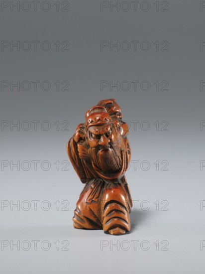 Netsuke in the shape of Shoki and an oni; maker, Japanese, Edo period 1st half of the 19th century; carved netsuke sculpture; subject: Shoki mythological figure and a demon; materials: carved netsuke; dimensions: height 4.5 cm, width 3.0 cm., A small carved figurine with a polished brown and reddish-brown surface depicting a bearded man wearing a rounded hat and flowing garments, shown from the front with a pronounced facial expression and detailed carved hair and beard, standing on a base formed by the folds of his clothing; the background is a smooth gradient of gray tones.