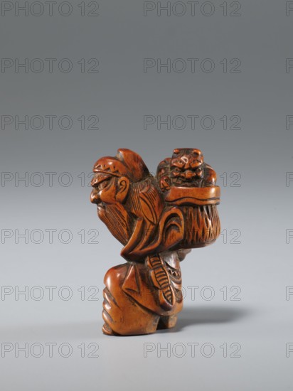 Netsuke in the shape of Shôki and an oni; maker, Japanese; Edo period 1603–1868, 1st half of the 19th century; materials: carved netsuke sculpture; subject: Shôki mythology and a demon oni; dimensions: height 4.5 cm, width 3.0 cm; function: figurine/netsuke., A small carved figure in warm brown and reddish-brown tones sits against a smooth gray background; the carving depicts an elderly bearded man with a pronounced nose and detailed facial lines, wearing a hat and carrying a textured basket or bundle on his back that holds a compact carved creature with a rounded face and prominent features; the figure shows carved patterns on clothing and hair, with darker brown recessed lines emphasizing the details and lighter brown highlights on raised surfaces, and a soft shadow falls beneath the sculpture on the gray surface.