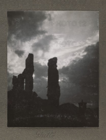Warsaw 1945 Ghetto, Bulhak, Jan 1876-1950 photographer, Warsaw Masovian Voivodeship, ghettos, ruins, Year 1945, World War II 1939-1945, 1945, Warsaw place of creation, album page, photograph, photographic print: height 14.7 cm, width 11.5 cm, album page: height 23.5 cm, width 18.0 cm, A grayscale image showing a dark silhouette of tall, irregular rock or ruin formations against a cloudy sky, with a large bright area behind the central silhouette creating contrast; the lower portion is dark with shadowed terrain and a few smaller jagged shapes, and the overall visible colors are shades of black, white, and gray.