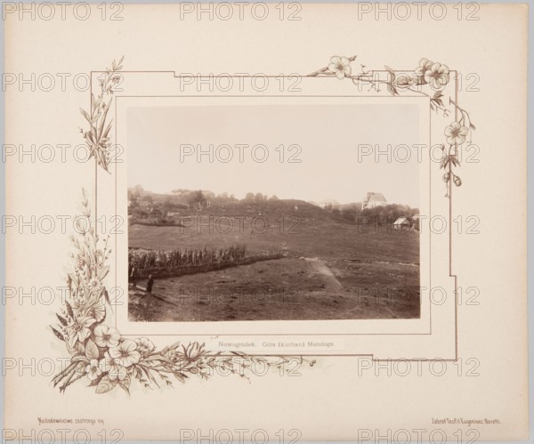 Nowogródek. Mindaugas Mountain Mound. Album card with photographic print glued onto lithographed cardboard. Photography from nature, print height 16.3 cm, width 22.5 cm; album card height 33.0 cm, width 39.8 cm. 1894. Subjects/notes: landscapes; mounds; Mindaugas Mountain Nowogródek; Nowogródek Belarus; Lithuania; Minsk; Adam Mickiewicz; makers/authors: Józef Mikolaj Boretti photographer, Teofil Eugeniusz Boretti compiler/author., A sepia-toned photograph shows a wide open grassy landscape with gently rolling hills, a group of taller plants or crops forming a line across part of the midground, and a few small buildings or houses visible on the distant hillside; near the foreground a solitary figure stands beside the planted row. The photo is mounted on a pale beige mat decorated with an ornate floral border featuring drawn flowers and leaves in brown and cream tones at the corners and along the sides. The overall visible colors are sepia, beige, brown, and cream.