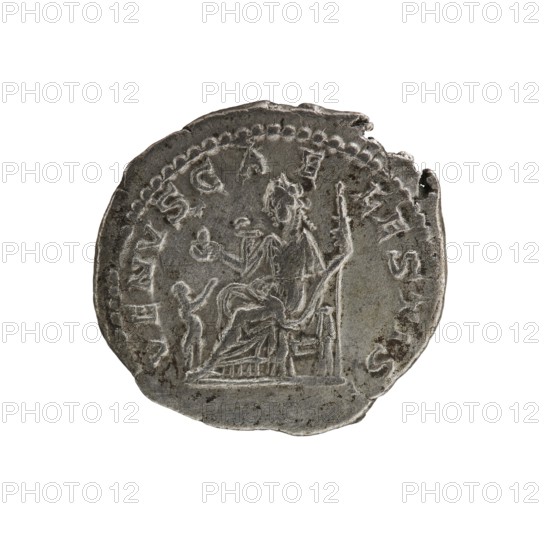 Denarius, Elagabalus Roman emperor 218–222. Issued under Julia Soaemias Augusta 218–222. Obverse: IVLIASOAEMIASAVG — Draped bust of Julia Soaemias facing right, pearl border. Reverse: VENVSCAELestis — Venus seated on a throne facing left, holding an apple in her right hand and a sceptre in her left; at her feet a child with outstretched arms, pearl border. Rome, 218–222. Coin; diameter ~18.0–19.5 mm; weight 2.55 g., A round, worn metal coin in shades of gray and silver with darker gray areas and slight brownish spots, showing a raised, circular beaded border and a central scene of a seated figure facing right on a throne, draped clothing visible, with an upright object beside the throne and a smaller standing figure near the seated figure; the coin edge is irregular and slightly chipped in places, and overall surface shows scratches and pitted texture.