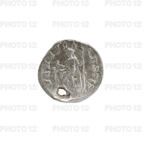 Denarius with hole, Elagabalus 204–222; Roman emperor 218–222. Issuer: Julia Soaemias 180–222; Augusta 218–222. Obverse: IVLIASOAEMIASAVG — draped bust of Julia Soemias facing right, pearl border. Reverse: VENVSCAELESTIS — Venus seated on a throne facing left, holding an apple in her right hand and a sceptre in her left; at her feet stands a child with outstretched arms, pearl border. Date: 218–222. Place of origin: Rome, Roman Empire. Coin: diameter ~17–18 mm, weight 2.35 g., A round, worn metallic object with an uneven edge and a small irregular hole near one side, showing a raised, indistinct figure or motif in low relief; the surface appears textured and scratched with areas of brighter and darker silver-gray tones against a white background.
