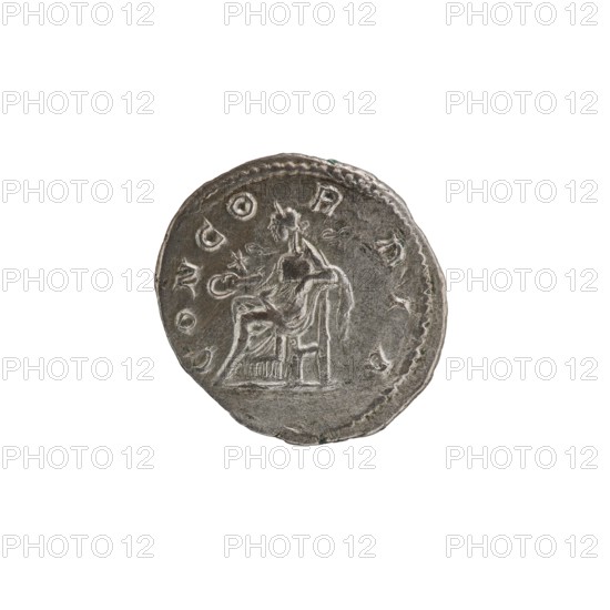 Denarius, Elagabalus Roman emperor 218–222 issuer; Julia Paula ca. 190–235; Roman empress 219–220 — Roman Empire, Rome, 219–220. Obv.: IVLIAPAVLAAVG. Draped bust of Julia Paula facing right, pearl rim. Rev.: CONCORDIA. Concordia seated left, holding a patera in her right hand, resting her left elbow on the back of the throne; a star in the left field, rim pearl. Coin; diameter approx. 18.5–19.0 mm; weight 3.00 g., A round metallic object with an uneven edge sits against a white background; the object has a worn silver-gray surface with darker gray shadows and a few small greenish spots. The surface shows a raised central scene of a seated human figure with draped clothing and a nearby vertical element suggesting a chair, and decorative raised shapes and circular motifs around the rim. The overall colors visible are silver-gray, darker gray, white background, and hints of green.