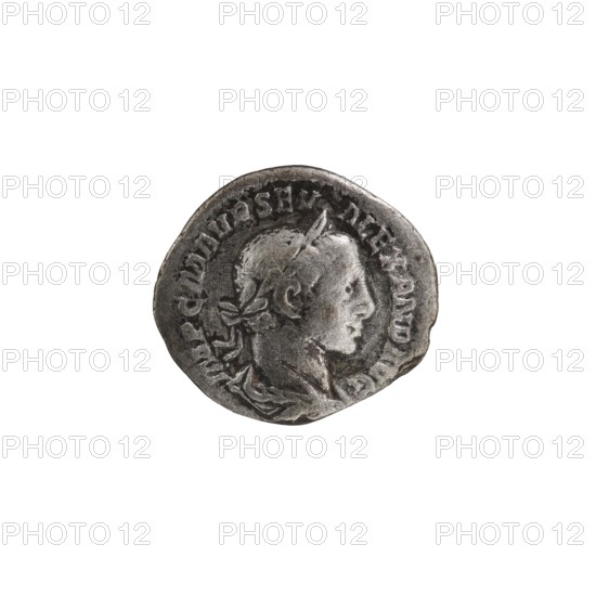 Denarius; personifications; Virtus personification; Alexander Severus Roman emperor, reign 222–235 — iconography. Obverse: IMPCMAVRSEV ALEXANDAVG. Bust of Alexander Severus with laurel wreath and paludamentum facing right; beaded border. Reverse: VIRTVSAVG. Virtus in military garb and helmet facing right, holding a spear point down in his right hand, resting his left hand on a shield at his feet; beaded border. Date: 222–228. Place of origin: Rome, Roman Empire. Medium: coin. Diameter: 17.0–19.0 mm. Weight: 2.80 g., A round, worn metallic coin with a raised profile of a person facing right at its center; the person appears to be wearing a laurel wreath or headband and has short hair and a defined jawline. The coin's surface shows textured wear and darker tarnished areas contrasted with lighter silvery highlights. Around the edge of the coin there is a raised rim with the suggestion of decorative or patterned markings. The overall colors visible are silver, gray, and darker charcoal ton...