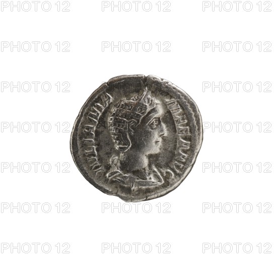 Denarius depicting Julia Mamaea ca. 180–235; Augusta 222–235 and Alexander Severus 208–235; Roman emperor 222–235. Obverse: busts/portraits of Julia Mamaea and Alexander Severus. Reverse: Fecunditas personification. Iconography dated 225–235, Roman Empire; Rome mint. Coin; diameter 18.5–19.5 mm, weight 3.07 g., A round metallic coin with a worn surface showing a raised profile of a person facing right; the figure appears to wear a detailed helmet or headdress and a draped garment at the neck. The coin's edge is irregular and slightly dented in places. Visible colors include silver-gray tones on the coin, with darker gray areas in the recesses and lighter highlights on the raised surfaces, set against a plain white background.