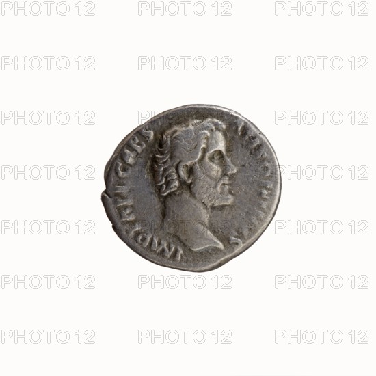 Denarius, Hadrian 76–138; Roman emperor 117–138 and Antoninus Pius 86–161; Roman emperor 138–161. Obverse: Head of Antoninus Pius without a cap to the right, legend IMP T AEL CAES - ANTONINVS around. Reverse: Diana stands to the right, holding a bow in her outstretched left hand and a lowered arrow in her right; legend TRIB PO - T COS around. Iconography: Diana; attributes: bow, arrows. Date: 138. Place of origin: Rome, Roman Empire. Coin type: denarius; diameter ~16.5–18.0 mm; weight 2.88 g; axis 195°., A circular metallic coin with a worn surface showing a raised profile of a bearded man facing to the right, the profile includes detailed hair, ear, eye, nose, lips, and a short neck; the coin has an irregular edge and a textured rim with shallow raised markings around the portrait; visible colors include shades of grey, silver, and darker grey patina across the surface, with subtle lighter highlights on the raised areas.