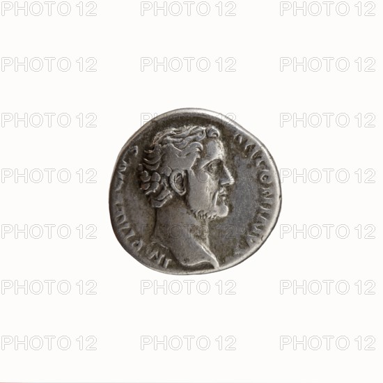 Denarius, Hadrian 76–138; Roman emperor 117–138 issued under Antoninus Pius 86–161; Roman emperor 138–161, caesar 138. Obverse: Head of Antoninus Pius bare, right, legend IMP T AEL CAES - ANTONINVS. Reverse: Concordia standing left, right hand outstretched holding a patera, left hand resting on a slender column and holding a double cornucopia; columns and personifications; inscriptions TRIB - POT COS. Roman, 138. Rome mint. Silver coin; diameter 16.0–16.5 mm, weight 3.37 g, axis 180°., A round metallic coin with a worn silver-gray surface showing a raised profile of a man facing right with short curly hair and a trimmed beard, set against a plain light background; the coin edge has uneven ridges and the portrait area displays darker gray shadows and lighter gray highlights.