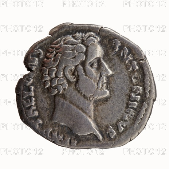 Denarius, Hadrian 76–138; Roman emperor 117–138 issuer, Antoninus Pius 86–161; Roman emperor 138–161 caesar 138. Obverse: Head of Antoninus Pius bare, facing right, legend IMP T AEL CAES - ANTONINVS. Reverse: Concordia standing left; in her outstretched right hand a patera, in her left hand a cornucopia resting on a slender column, legend TRIB POT - COS. Iconography: Concordia, columns, personifications, cornucopias, paterae. Date: 138. Place of origin: Rome, Roman Empire. Object type: coin denarius. Diameter: 17.0–18.0 mm. Weight: 3.30 g. Axis: 195°., A worn round coin with a raised profile of a bearded man facing right, showing detailed hair curls and facial features, in metallic gray and dark silver tones with areas of darker tarnish and lighter highlights; the coin edge is irregular and slightly chipped in places, with textured relief around the portrait and faint decorative markings along the rim.