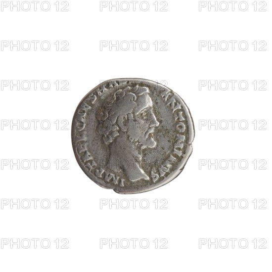 Denarius of Antoninus Pius 86–161; Roman emperor 138–161. Obverse: Head of Antoninus Pius uncovered, facing right; legend IMP T AEL CAES HADRI - ANTONINVS. Reverse: Diana standing to the right, holding a bow in her outstretched left hand and an arrow in her lowered right hand; legend AVG PIVS PM TR - P COS DES II. Roman silver coin, struck 138. Diameter 16.0–17.0 mm, weight 3.31 g, axis 195°., A small round metallic object with a worn, textured surface showing a raised profile of a man's head in profile facing right, with short hair and a beard, surrounded by a raised border; the metal appears silver-grey with darker grey and greenish tarnish in places.