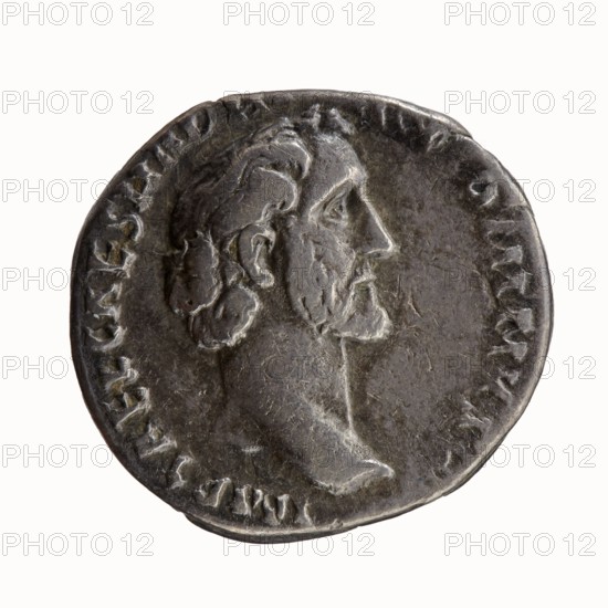 Denarius of Antoninus Pius 86–161; Roman Emperor 138–161. Obverse: Head of Antoninus Pius uncovered to the right, legend IMP T AEL CAES HADRI - ANTONINVS. Reverse: Diana standing to the right, holding a bow in her outstretched left hand and an arrow in her lowered right hand, legend AVG PIVS PM T - RP COS DES II. Iconography: Diana standing; attributes: bow, arrows. Issuer: Antoninus Pius. Date: 138. Place of mint: Rome. Roman Empire 27 BC–476. Coin; denarius. Diameter: 17.0–18.0 mm. Weight: 2.58 g. Axis: 180 degrees., A round metallic coin with a worn surface showing a raised profile of a bearded man facing right; the coin appears mostly dark gray with lighter gray highlights on the raised areas and some subtle brownish tones in recessed parts; a ring of raised decorative marks circles the portrait near the edge; the portrait shows textured hair, an ear, a prominent nose, and a defined neck and chin; the background around the portrait is smoother and slightly darker than the highlight...