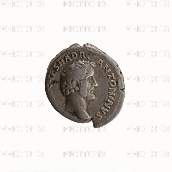 Denarius, Antoninus Pius 86–161; Roman emperor 138–161. Obverse: head of Antoninus Pius uncovered to the right; legend IMP T AEL CAES HADRI-ANTONINVS. Reverse: Minerva standing left, in her outstretched right hand she holds Victoria, in her lowered left hand she holds a spear with the head pointing upwards and a shield resting on the ground; legend AVG PIVS PM - TRP COS DES II. Iconography: Minerva with Victoria and spear; Victoria attribute; spears. Date: 138. Place of origin: Rome, Roman Empire. Type: coin denarius. Diameter: 17.0–18.5 mm. Weight: 3.01 g. Axis: 180°., A single round coin with a raised profile of a man's head facing right, showing facial hair and wavy hair, with textured surface and some dents and chips along the edge; the coin appears in shades of gray and silver with darker gray patina in recessed areas and slight brownish tones in spots, set against a plain white background.