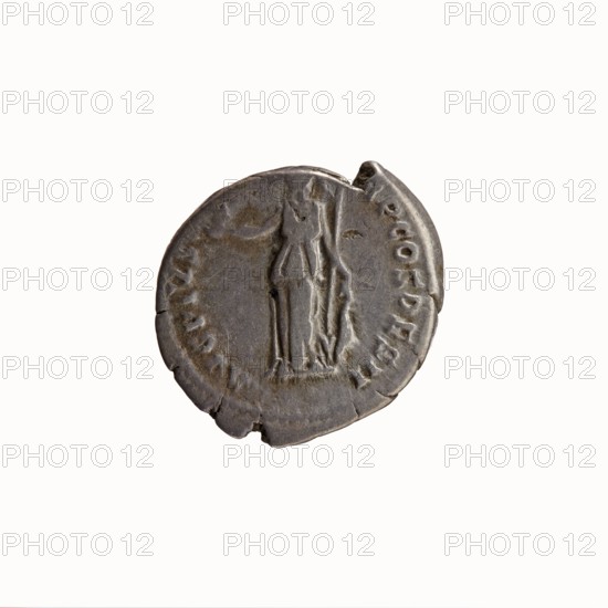 Denarius, Antoninus Pius 86–161; Roman emperor 138–161. Obverse: Head of Antoninus Pius uncovered, facing right; inscription: IMP T AEL CAES HADRI - ANTONINVS. Reverse: Minerva standing left, holding Victoria in her outstretched right hand and a spear in her lowered left hand with the spearhead pointing upwards; a shield rests on the ground; inscription: AVG PIVS PM TRP COS DES II. 138 CE, Roman Empire; Rome mint. Coin. Diameter 17.0–18.5 mm, weight 3.01 g, axis 180°., A circular metal object with a weathered, uneven edge and a dull gray surface sits against a plain white background; the object shows a raised, central vertical figure with flowing contours and adjacent raised shapes suggesting drapery, and there are several irregular chips and small cracks along the rim; colors visible include shades of gray, darker gray shadows, and hints of brownish patina.