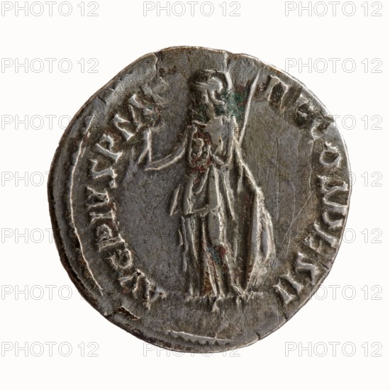 Denarius; Antoninus Pius 86–161; Roman emperor 138–161 — issuer. Obverse: head of Antoninus Pius uncovered to the right; legend IMP T AEL CAES HA DRI ANTONINVS. Reverse: Minerva standing left, in her outstretched right hand she holds Victoria, in her lowered left hand she holds a spear with the head pointing upwards and a shield resting on the ground; legend AVG PIVS PM T RP COS DES II. Iconography: Minerva, Victoria, spears, shields, ancient deities. Date: 138. Place of origin: Rome, Roman Empire. Object type: coin denarius. Dimensions: diameter 17.0–17.5 mm; weight 3.44 g; axis 180°., A circular metal coin photographed against a white background showing a worn raised relief of a standing human figure wearing a draped garment and helmet, holding a long vertical staff in one hand and a small object in the other; the coin surface appears scratched and weathered with areas of darker and lighter gray, small patches of brown and green discoloration, and a slightly irregular rim.