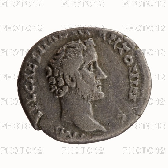 Denarius, Antoninus Pius 86–161; Roman Emperor 138–161. Obverse: Head of Antoninus Pius uncovered to the right, inscription IMP T AEL CAES HADRI ANTONINVS. Reverse: Minerva standing left; in her outstretched right hand she holds Victoria, in her lowered left hand she holds a spear with the head pointing upwards and a shield resting on the ground, inscription AVG PIVS PM TRP COS DES II. 138 CE. Rome, Roman Empire. Coin; diameter 16.0–18.0 mm, weight 3.09 g, axis 180°., A worn round coin with a raised profile of a bearded man facing right, showing detailed hair and facial features; the coin surface is a mottled dark gray with lighter gray highlights and some brownish tones, with uneven edges and areas of wear; a faint raised border and remnants of raised markings encircle the portrait, and the background is plain white.