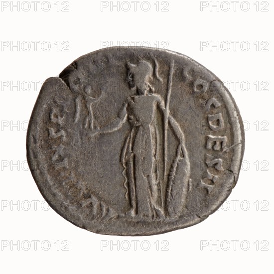Denarius, Antoninus Pius 86–161; Roman Emperor 138–161. Obverse: Head of Antoninus Pius uncovered to the right, legend IMP T AEL CAES HADRI ANTONINVS. Reverse: Minerva standing left, in her outstretched right hand she holds Victoria, in her lowered left hand she holds a spear with the head pointing upwards and a shield resting on the ground, legend AVG PIVS PM TRP COS DES II. Date: 138. Place of origin: Rome, Roman Empire. Coin; diameter 16.0–18.0 mm; weight 3.09 g; axis 180°., A round, worn coin with a dark gray to brown patina showing a standing figure in profile wearing a long draped garment and holding a long staff; a group of faint raised marks and shallow relief shapes appear around the coin’s edge; the surface shows irregularities, small dents, and areas of smoother wear.