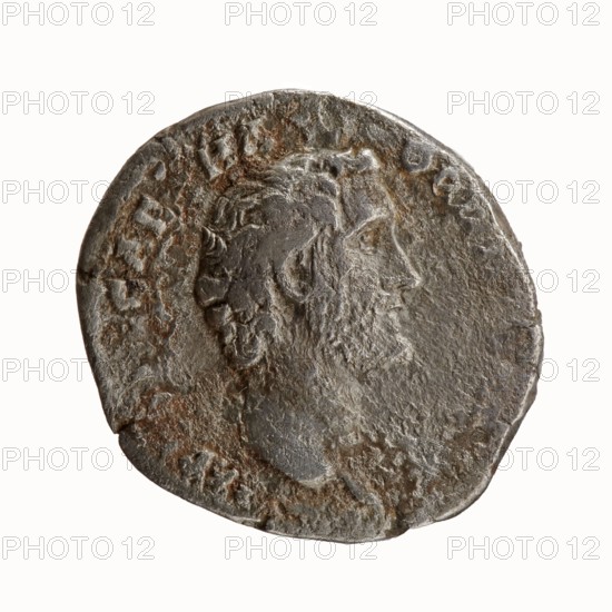 Denarius, Antoninus Pius 86–161; Roman Emperor 138–161 issuer. Obverse: Head of Antoninus Pius bare, right; legend IMP T AEL CAES HA DRI ANTONINVS. Reverse: Minerva standing left, holding Victoria in her outstretched right hand and a spear in her lowered left hand spear head upward, shield resting on the ground; legend AVG PIVS PM TR P COS DES II. Date: 138. Place of origin: Rome, Roman Empire. Media: coin. Diameter: 16.0–18.0 mm. Weight: 2.81 g. Axis: 180°., A worn round coin with an uneven edge showing a raised profile of a bearded man facing right; the surface has textured, pitted areas and patches of darker brownish rust and lighter gray metal tones, with a few smoother, slightly shiny spots and an overall aged, tarnished appearance.