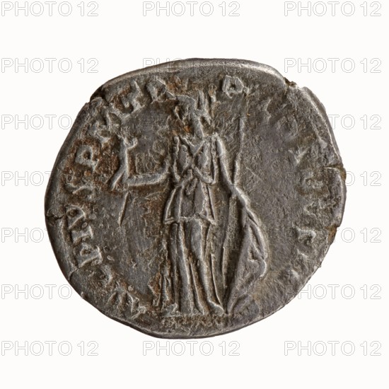 Denarius, Antoninus Pius 86–161; Roman Emperor 138–161. Obverse: head of Antoninus Pius bare, right; inscription IMP T AEL CAES HA - DRI ANTONINVS. Reverse: Minerva standing left, in her outstretched right hand she holds Victoria, in her lowered left hand she holds a spear with the head pointing upwards and a shield resting on the ground; inscription AVG PIVS PM TR - P COS DES II. Date: 138. Place of origin: Rome, Roman Empire. Medium: coin; diameter 16.0–18.0 mm; weight 2.81 g; axis 180°. Subjects/iconography: Minerva, Victoria, spears, shields; ancient deities; issuer: Antoninus Pius., A round metallic object with a worn, uneven surface showing a raised, central figure of a standing person holding an object in one hand and a draped cloth in the other, surrounded by a ring of low-relief markings; the metal appears dark gray with areas of lighter gray highlights and patches of brownish discoloration, and the edges are irregular and slightly damaged.