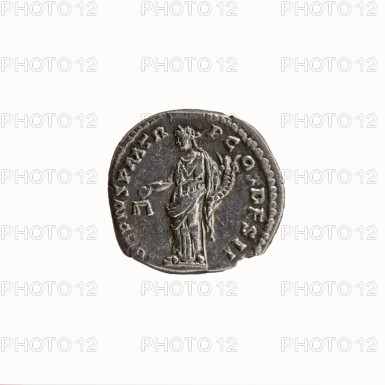 Denarius, Antoninus Pius 86–161; Roman Emperor 138–161. Obverse: head of Antoninus Pius uncovered to the right, legend IMP T AEL CAES HAD - RI ANTONINVS around. Reverse: Aequitas standing left, holding scales in his outstretched right hand and a cornucopia in his left, legend AVG PIVS PM TR - P COS DFS sic! II around. Iconography: Aequitas, scales, cornucopia, personification. Date: 138. Place: Rome, Roman Empire. Medium/function: coin denarius. Diameter: 16.0–17.5 mm. Weight: 2.92 g. Axis: 180°., A round metallic coin with a worn, uneven edge shown against a white background, featuring a raised relief of a robed standing figure holding an object in one hand and a curved, decorated staff or cornucopia in the other; the surface is dark gray with lighter gray highlights on the raised areas and subtle brownish tarnish in places, and there is a ring of raised dots near part of the rim.