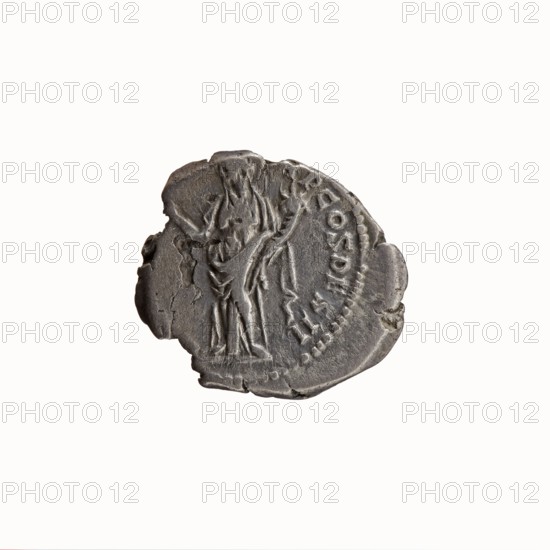 Denarius, Antoninus Pius 86–161; Roman emperor 138–161. Obverse: Head of Antoninus Pius uncovered to the right, legend IMP T AEL CAES HADRI - ANTONINVS around. Reverse: Felicitas standing to the left, holding a caduceus in her outstretched right hand and a cornucopia in her left, legend AVG PIVS PM T - RP COS DES II around. Iconography: personifications, caduceuses, cornucopias, Felicitas. Date: 138. Place of origin: Rome, Roman Empire. Object type: coin denarius. Dimensions: diameter 16.5–18.5 mm; weight 3.03 g; axis 190°., A worn round metal object with an uneven, slightly chipped edge shown against a white background, appearing in shades of gray and dark gray with areas of lighter gray highlighting raised details; the surface shows a relief of a standing human figure draped in flowing garments and holding an object, with textured lines suggesting folds and hair, and a curved band of raised dots and short marks following the contour near one side.