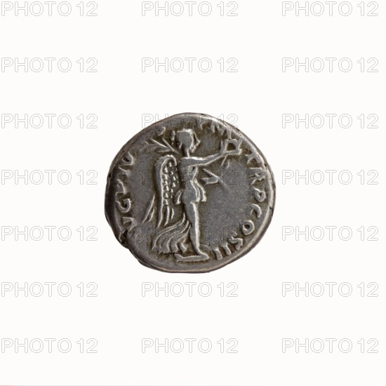 Denarius, Antoninus Pius 86–161; Roman Emperor 138–161. Obverse: head of Antoninus Pius bare, right, legend IMP T AEL CAES HADR ANTONINVS around. Reverse: Victoria walking right, holding a wreath in her outstretched right hand and a palm branch in her left, legend AVG PIVS PM TR P COS II around. Date: 139. Place: Rome, Roman Empire. Iconography: personifications Victoria, wreaths, palm branches. Medium: silver coin. Dimensions: diameters 15.0 mm / 17.0 mm, weight 3.88 g, axis 180°., A round metallic object with a worn surface in shades of gray and dull silver, showing a raised relief of a standing winged figure facing sideways with an outstretched arm and flowing drapery, surrounded by a ring of small raised marks and irregular edges.
