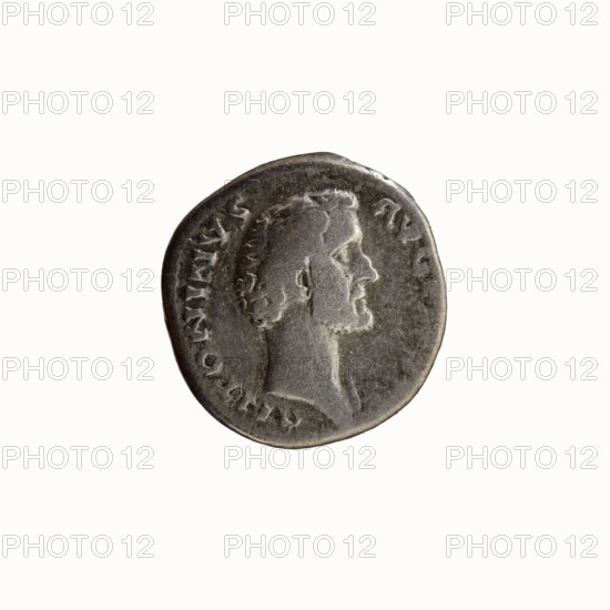 Denarius of Antoninus Pius 86–161; Roman emperor 138–161. Obverse: Head of Antoninus Pius without a cover to the right, legend ANTONINVS - AVG PIVS PP. Reverse: Sacred implements, from the left: sprinkler aspergillum, jug capis, crosier lituus and scoop simpulum, legend TR P COS II around. Date: 139. Place of origin: Rome, Roman Empire. Coin: diameter 16.5–17.0 mm, weight 3.08 g, axis 195°., A circular coin with a worn metallic surface showing a raised profile of a man's head in side view; the head has short curly hair and a short beard, and the neck and shoulders are partially visible. The coin's rim is uneven and shows texture and wear. The visible colors are shades of gray, dark gray, and hints of silver, with subtle darker areas around the relief and edges.