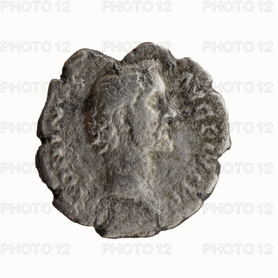 Denarius, Antoninus Pius 86–161; Roman emperor 138–161 — obverse: head of Antoninus Pius bare, facing right, legend ANTONINVS·AVG·PIVS·PP; reverse: sacred implements from left — aspergillum, jug capis, crosier staff lituus, and scoop simpulum, legend TR P COS II, dated 139; Rome, Roman Empire; coin; diameter ~18.0–18.5 mm; weight 2.51 g; axis 180°., A worn circular metallic object with an irregular scalloped edge, showing a raised profile of a person's head in profile facing right; the surface is rough and textured with patches of lighter and darker tones creating a mottled appearance. The colors visible are various shades of gray, silver, and darker charcoal, with some areas that appear slightly reflective and others that look matte. The background is pale and neutral, contrasting with the metallic object.