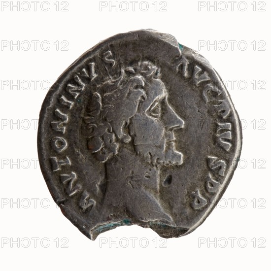 Denarius of Antoninus Pius 86–161; Roman emperor 138–161. Obverse: Head of Antoninus Pius uncovered to the right, legend ANTONINVS · AVG · PIVS · PP. Reverse: Pax standing left, holding a twig in his right hand and a cornucopia horn of plenty in her left, legend TR · POT · COS II. Iconography: Pax, personification, twigs, cornucopia. Roman, Rome, 139. Silver coin; diameter 17.0–17.5 mm, weight 2.88 g, axis 180°., A circular metallic object with a worn, uneven edge showing a profile of a person's head facing right; the head has short curly hair and a beard, and the surface shows scratches and small dents. The metal appears gray with darker and lighter areas and small patches of greenish corrosion near the rim. There is a raised decorative border and a ring of carved impressions around the head, and the background is a pale off-white.