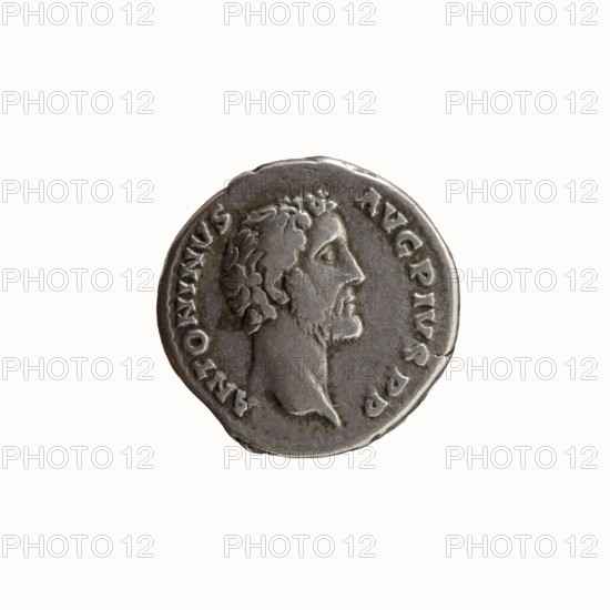 Denarius of Antoninus Pius 86–161; Roman Emperor 138–161. Obverse: Head of Antoninus Pius uncovered, facing right, legend ANTONINVS • AVG • PIVS • PP. Reverse: Container modius with ears of corn and poppy head, legend TR • POT • COS II. Minted Rome, 139. Silver coin; diameter 17.5 mm; weight 3.58 g; axis 165°., A circular metallic coin with a raised profile of a bearded man facing right in the center, surrounded by a raised rim and a ring of small embossed marks; the coin appears silver-gray with darker gray shadows in recessed areas and slightly lighter highlights on raised surfaces, and shows surface wear and minor irregularities along the edge.
