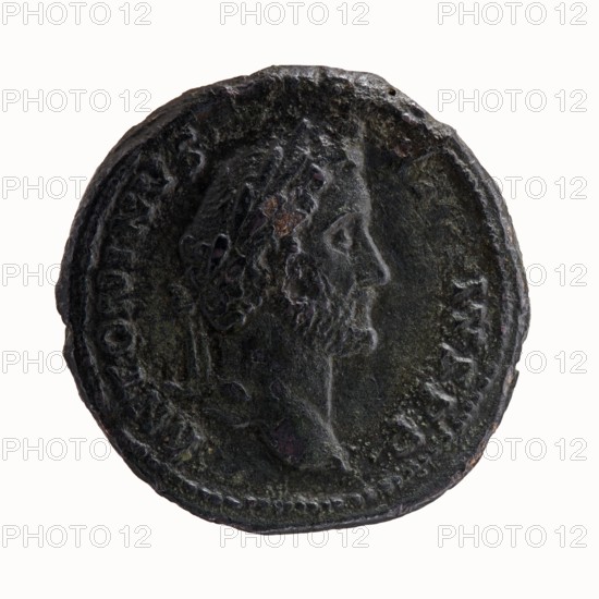 Head of Antoninus Pius with laurel wreath to the right, inscription ANTONINVS - AVG PIVS PP around; reverse: Bust of young Marcus Aurelius, in cloak paludamentum and bare to the left, inscription AVRELIVS CAES AVG PII F COS DES all around, under the portrait SC., dated 139. Roman Empire 27 BC–476, Rome. Coin; diameter 29.0–29.5 mm, weight 12.95 g, axis 180°. Subjects: Antoninus Pius 86–161; Roman emperor 138–161, Marcus Aurelius 121–180; Roman emperor 161–180; caesar 139–161, iconography of heads portraits, paludamentums., A round dark metal coin with a worn raised profile of a bearded man facing right, showing textured hair and facial features; the coin surface has uneven patina with dark green, black, and brown tones and small areas of lighter greenish and reddish discoloration; a raised border encircles the edge and there are traces of raised elements and worn decoration around the portrait.