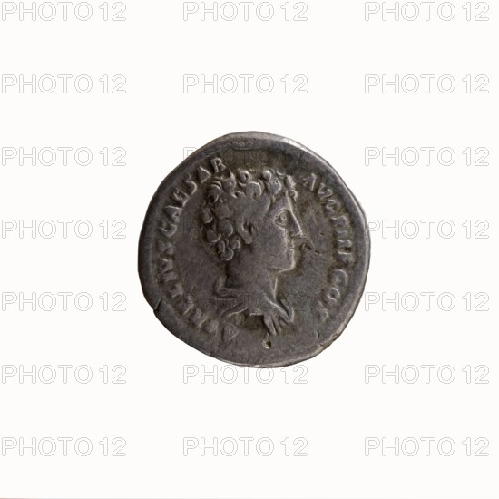 Denarius, Antoninus Pius 86–161; Roman emperor 138–161 issuer Marcus Aurelius 121–180; Roman emperor 161–180 caesar 139–161. Obverse: Head of Antoninus Pius without a cap to the right, legend ANTONINVS AVG PIVS PP TR P COS III. Reverse: Bust of young Marcus Aurelius without a cap, wearing a cloak paludamentum, facing right, legend AVRELIVS CAESAR AVG PII F COS. Date: 140. Place of origin: Rome, Roman Empire. Coin; diameter 16.5–17.5 mm, weight 3.38 g, axis 345°., A round metallic coin with a worn surface showing a raised profile of a person's head facing right, with curly hair and a visible neck and shoulder drapery; the coin appears mostly gray with darker gray and subtle brownish patina areas, and faint greenish discoloration near the lower edge; the rim is slightly irregular and the background around the coin is off-white.