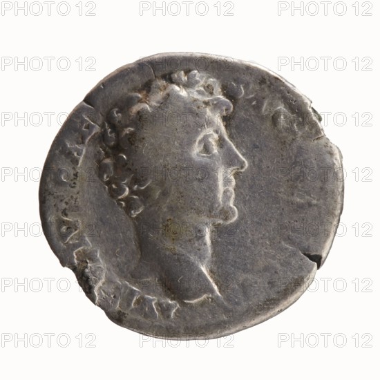 Denarius; obverse: head of Antoninus Pius with laurel wreath facing right, inscription ANTONINVS AVG PI - VS PP TR P COS III around; reverse: head of young Marcus Aurelius without covers right, inscription AVRELIVS CAE - SAR AVG PII F COS around. Issuer: Antoninus Pius 86–161 CE; Roman emperor 138–161 with Marcus Aurelius 121–180 CE; caesar 139–161, heir to the throne. Date: 140 CE. Roman Empire; Rome mint. Coin. Diameters: 16.0 mm, 18.5 mm; weight 2.78 g; axis 225°., A worn circular metallic object with a raised profile of a person's head in right-facing profile, showing curly hair and a visible neck and shoulder; the surface appears aged with scratches, nicks, and small pits, and a few chipped edges; the overall color is silvery gray with areas of darker gray tarnish and small patches of brownish discoloration; the background behind the object is a pale off-white.