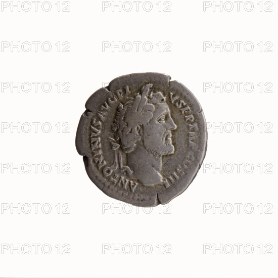 Denarius, Antoninus Pius 86–161; Roman emperor 138–161. Obverse: Head of Antoninus Pius with laurel wreath to the right, legend ANTONINVS AVG PI·VS PP TR P COS III. Reverse: Head of young Marcus Aurelius without a covering to the right, legend AVRELIVS CAESAR AVG PII F COS. Dated 140. Roman Empire, Rome. Coin; diameter 17.0–17.5 mm, weight 3.18 g, axis 210°., A circular metallic object with a worn, dark gray surface featuring a raised profile of a man facing right; the man has short hair, a beard, and a laurel-like headpiece. The object's edge is irregular with several small notches and chips. The background is plain and light, creating contrast with the metallic gray of the object.