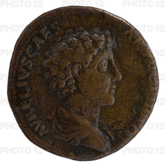 Sestertius, Marcus Aurelius 121–180; Roman emperor 161–180. Obverse: Bust of young Marcus Aurelius in paludamentum, without headgear, right; legend AVRELIVS CAES AR AVG PII F COS. Reverse: Sacred utensils from the left: knife secespita, sprinkler aspergillum, jug capis, crosier lituus and dipper simpulum; legend PIETAS AVG, in section SC. Issued during Antoninus Pius 86–161; Roman emperor 138–161 ca. 140–144. Rome, Roman Empire 27 BC–476. Coin; weight 23.72 g; diameter 32.0 mm; axis 180°., A round worn coin with a raised profile of a person facing right, showing curly hair, an ear, a prominent nose, and a visible neck and shoulder drapery; the coin surface is textured with uneven wear and small dark spots, and the rim is irregular; visible colors include shades of brown, dark brown, and hints of black.
