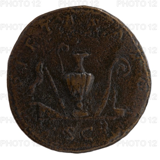 Sestertius, Marcus Aurelius 121–180; Roman emperor 161–180 as Caesar 139–161; issuer: Antoninus Pius 86–161; Roman emperor 138–161. Obverse: Bust of young Marcus Aurelius in paludamentum, without headgear, right; inscription AVRELIVS CAES · AR AVG PII F · COS. Reverse: Sacred utensils, from the left: knife secespita, sprinkler aspergillum, jug capis, crosier lituus and dipper simpulum; inscription PIETAS AVG; in section SC. Date: ca. 140–144. Place: Rome, Roman Empire. Object type: coin sestertius. Diameter: 32.0 mm. Weight: 23.72 g. Axis: 180°., A round, worn coin with a dark brown and black patina, showing a central raised shape that resembles a vessel or urn flanked by a few curved decorative elements; the surface has pitted and uneven texture with lighter brown highlights on raised areas and darker brown to near-black recesses; the coin edge is irregular and shows spots of lighter brown wear.