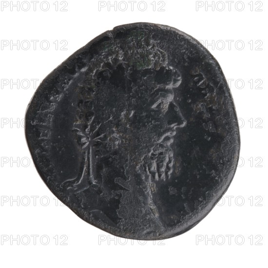 Sestertius of Lucius Verus 130–169; Roman emperor 161–169. Obverse: Head of Lucius Verus in laurel wreath facing right, legend LAVREL VERVS AVG Armeniacus all around. Reverse: Mars walking right, holding a spear in his right hand and a trophy in his left, legend TRP IIII – IMP II COS II with control letters S–C in fields. Date: 163–164. Rome, Roman Empire. Bronze coin; diameter 30.5–31.5 mm, weight 20.75 g, axis 345°., A dark round object with an irregular edge shows a raised profile of a person's head facing right; the head has textured hair and a beard. The surface is worn and uneven with areas of smooth sheen and rough patches. A small stylized plant-like shape appears near the lower left of the profile. The visible colors are dark gray and black with hints of lighter gray.