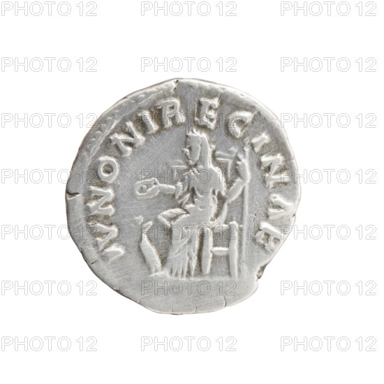 Denarius depicting Faustina the Younger ca. 130–176; Roman empress 161–176 and Marcus Aurelius 121–180; Roman emperor 161–180 as issuer. Obverse: Bust of Faustina II in drapery facing right, legend FAVSTINA - AVGVSTA. Reverse: Juno veiled, seated left, holding a patera in her right hand and a scepter in her left, a peacock at her feet left, legend IVNONI REGINAE. Date: 161–176. Place: Rome, Roman Empire. Coin: silver denarius; diameter 17.5 mm; weight 3.25 g; axis 180°., A round metallic object with a silver color, showing a raised depiction of a seated human figure facing slightly to the left and holding a circular item in an outstretched hand, with a staff or long object behind the figure and a small bird-like shape near the figure's feet; the surface shows circular ridges and worn, uneven edges with a few small cracks and dents, and the background surrounding the object is white.
