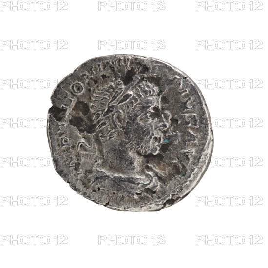 Denarius, Elagabalus reigned 218–222. Obverse: Bust of Elagabalus with a laurel wreath and paludamentum facing right; pearl border; legend IMP ANTONINVS PIVS AVG. Reverse: Elagabalus wearing a laurel wreath and long robe, standing left, holding a patera above an altar in his right hand and a scroll in his left, star at top in left field; pearl border; legend INVICTVS SACERDOS AVG. Roman Empire, Rome; 218–222. Coin; diameter ~27.5–28.5 mm; weight 2.97 g., A worn round metal coin with an uneven textured surface showing a raised side-profile portrait of a bearded man; the coin appears tarnished and aged with a mix of dark gray and lighter silver tones, small patches of greenish-blue corrosion, and areas of darker brownish-gray discoloration, set against a plain white background.