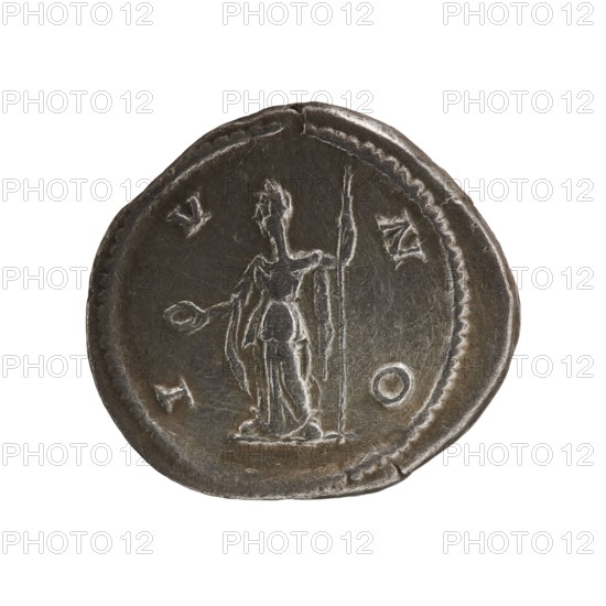 denarius, Julia Maesa ca. 160–224; Augusta 218–224, Juno myth., 218–222, coin; diameter 19.5–21.0 mm; weight 3.51 g, A round metallic object with a worn, uneven edge and a patina of dark gray and silver shows a raised figure in its center. The figure appears standing and holds a long vertical staff in one hand while the other hand is extended outward. The surface has shallow engraved lines and lightly raised borders, with areas of lighter silver highlights where the metal is more worn and darker gray recesses around the designs. The overall color palette is dark gray and silver with subtle variations in tone across the object.