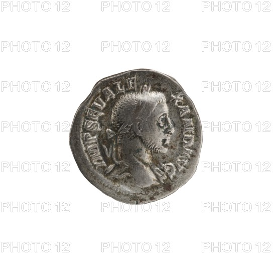 Denarius of Alexander Severus reigned 222–235 CE. Obverse: bust of Emperor Alexander Severus; Reverse: Victoria winged victory and inscription referencing Alexander Severus. Roman imperial coin, dated 228–231 CE, Rome. Bronze/silver, coin; diameter 19.0 mm; weight 2.91 g., A round metallic object with a worn, uneven edge showing a raised profile of a person facing right, featuring short textured hair and a short beard, with a tied ribbon or band at the back of the head; the surface shows areas of darker tarnish and lighter polished highlights in shades of silver, gray, and dark brown-green, with a few small pits and scratches across the face and rim.