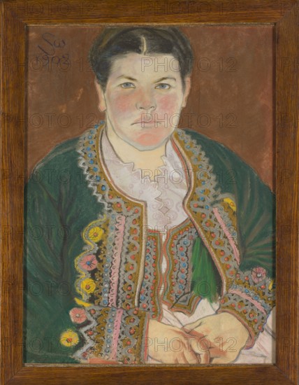 Portrait of his wife in a serdak, Wyspianski, Stanislaw 1869–1907 painter, female portraits, ethnography, Wyspianska, Teodora Teofila 1868–1957 – iconography, Krakowians, 1902, pastel, height 63 cm, width 47.3 cm, A framed portrait of a person with short dark hair and a pale face with rosy cheeks, shown from the torso up against a brown background. The person wears a green garment with elaborate embroidered trim featuring accents of yellow, pink, blue, and gold, and a white ruffled collar visible at the neckline. The hands rest in the lap and are rendered in light skin tones with subtle shading. The frame is wooden with a warm brown finish.