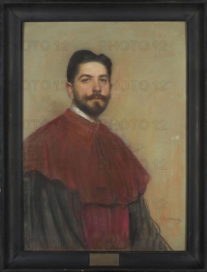 Portrait of professor Leon Krynski, painted by Leon Wyczólkowski 1852–1936. The portrait was painted in the year Krynski took up the chair at the Jagiellonian University, 1901, Kraków. Pastel, 97 × 69 cm. Style: Young Poland. Subject: male portrait professor Leon Krynski, b. 1866, bust., A framed portrait of a man wearing a dark red garment over a darker robe, with a white collar visible at the neck. He has dark hair, a mustache, and a beard, and his face shows natural skin tones against a warm, beige background. The frame is dark, and there is a small metallic plate at the bottom of the frame. Colors visible include red, dark gray or black, beige, white, brown, and hints of pink in the face.