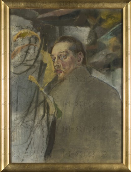 Self-portrait, Kazimierz Sichulski 1879–1942; after 1909; pastel drawing; height 76.8 cm, width 56.3 cm. Subject: self-portrait, male portrait. Style/medium: pastel; painter; Polish., A portrait painting of a man viewed from behind with his head turned to look over his shoulder, showing a pale face with blue eyes, light brown hair, and a small mustache and goatee; he wears a large coat in muted gray-green tones that covers most of his body. The background contains a mix of soft, diffuse shapes and organic forms, including a group of branches and a few leaflike shapes in yellow, orange, and green, set against areas of gray, brown, and dark green. The painting is set in a gold-colored frame with a simple beveled profile.