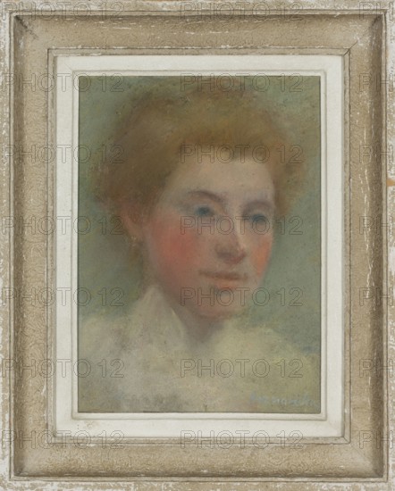 Portrait of a Young Woman, Olga Boznanska 1865–1940, pastel, female portrait, before 1914, painter, L'Union des femmes peintres et sculpteurs UFPS, women's art, female artists., A framed pastel portrait of a woman shown from the shoulders up, with soft, diffuse edges and muted coloring; she has light brown to reddish hair, pale skin with rosy cheeks, blue-gray eyes, and a gentle, neutral expression, wearing a light-colored garment that blends into a misty, green-gray background; the portrait sits within a narrow white mat and a textured, distressed frame in beige, tan, and off-white tones.