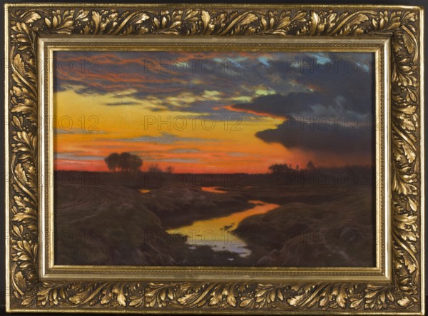 Landscape at Sunset, Jan Grubinski 1874–1945, painter. Pastel on paper, 1909. Subject: sunset landscape, nocturne; style: Symbolism, Young Poland. Medium: pastel; dimensions: height 30.2 cm, width 44.3 cm., testamentary bequest. Poland., A framed landscape painting showing a sunset sky with bands of yellow, orange, red, blue, and dark gray clouds above a darkened horizon; a winding reflective stream runs toward the foreground with golden and bluish reflections, bordered by dark brown and greenish landforms and grasses; a few silhouetted trees stand on the horizon; the painting is set in an ornate gold frame with carved leaf and scroll details and darker shadowed recesses.