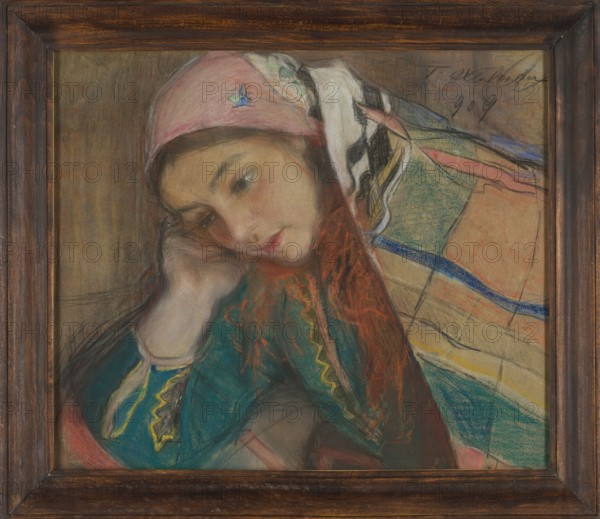Portrait of a Girl in Krakow Costume, Teodor Axentowicz 1859–1938. Pastel, 1909. Height 33.5 cm; width 44.5 cm. Female portrait of a peasant girl in a Krakow Cracovian costume with scarf headgear; Polish pastel painting in the Young Poland style; ethnographic subject; Krakow., A framed pastel portrait of a young woman leaning her head on her hand, wearing a pink headscarf and a colorful shawl; her face is rendered in soft flesh tones with rosy cheeks and red lips, and her hair shows reddish orange highlights. The shawl and clothing include teal, green, blue, yellow, black, white, peach, beige, and coral tones arranged in striped and patterned sections. The background is a muted brown. The frame is dark wood with visible grain.
