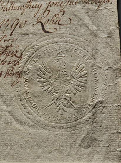 Round seal impression of the Civil-Military Commission of the Kraków Voivodeship. Polish eagle with a crown. In the rim the inscription: PIECZEC KOMMISSYI CYWIL : WOYSK : POWIATOW KRAK : Y : PROSZ., 1790, Poland, seal, The image shows a close-up of textured, off-white paper with an embossed circular seal depicting a heraldic eagle with outstretched wings and a crown; the seal creates raised and indented relief patterns on the paper. Around the seal are partial curved outlines and decorative border details pressed into the surface. In the upper left area there is handwritten ink visible in a dark brown color with flowing cursive strokes, and a few scattered ink marks extend toward the center. The paper surface exhibits creases, small tears, and areas of irregular texture and wear, with subtle variations in shading from pale beige to light gray. A narrow dark strip appears along the right edge.